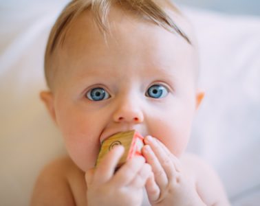 baby with blonde hair and blue eyes sucking on a block
